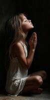 Child in prayer with closed eyes in a dimly lit room photo