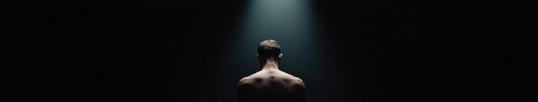 Man under a spotlight in a dark space during a moment of introspection photo