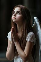 Young girl with angel wings praying in a dimly lit environment photo