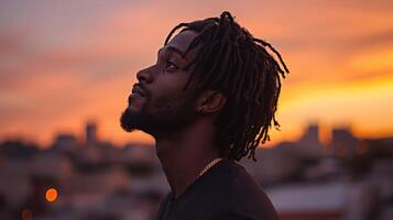 Man with dreadlocks gazes at sunset in urban skyline photo