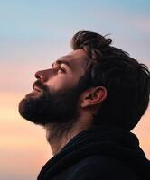 Man gazing thoughtfully at the sky during sunset in a tranquil setting photo