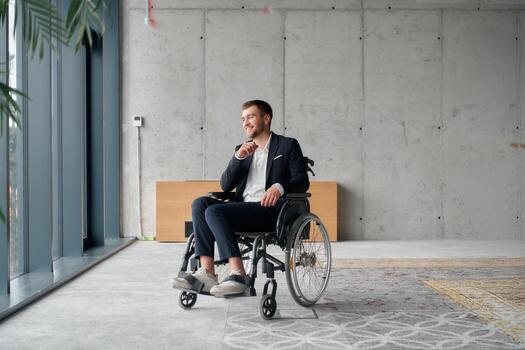 A director in a wheelchair sitting alone in an empty office, deeply reflecting on business strategies and decisions, contemplating the path forward with focused determination. photo
