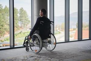 A director in a wheelchair sitting alone in an empty office, deeply reflecting on business strategies and decisions, contemplating the path forward with focused determination. photo