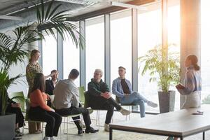 A diverse group of business professionals sits attentively in a modern office, actively participating in a training session led by an instructor, focusing on the latest technological advancements in photo