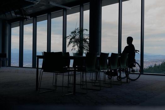 A director in a wheelchair sitting alone in an empty office, deeply reflecting on business strategies and decisions, contemplating the path forward with focused determination. photo