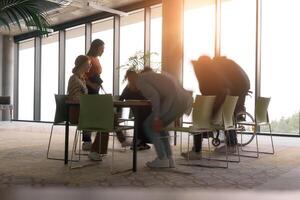 A diverse business team, working urgently around a conference table, collaborates on a meeting while their director, seated in a wheelchair, waits for their input photo