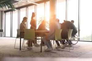 A diverse business team, working urgently around a conference table, collaborates on a meeting while their director, seated in a wheelchair, waits for their input photo