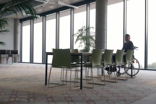 A director in a wheelchair sitting alone in an empty office, deeply reflecting on business strategies and decisions, contemplating the path forward with focused determination. photo