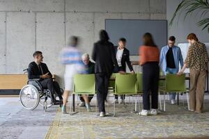 A diverse business team, working urgently around a conference table, collaborates on a meeting while their director, seated in a wheelchair, waits for their input photo