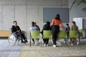 A diverse business team, working urgently around a conference table, collaborates on a meeting while their director, seated in a wheelchair, waits for their input photo