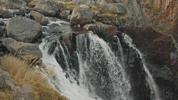 Rapid stream of icy water is hiding down, falling from top of cascade of waterfalls, in middle of rocks and stones covered with moss. video
