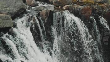 The rushing stream of a crystal-clear mountain river cascades over a black cliff, creating a stunning waterfall. Slow motion. video