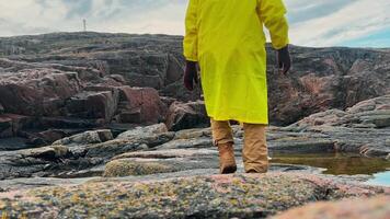 Waterproof, warm and comfortable boots allow solo tourist in bright clothing to stroll along rugged, rocky terrain wet from rain without unnecessary difficulty. video