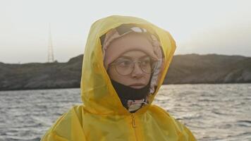 Teenage girl, wrapped in hooded jacket and wearing warm, waterproof clothing, is sailing on ship on windy day, in midst of northern seascape, beyond Arctic circle. video
