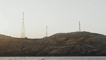 Several telecommunication radio towers stand on rocky island in middle of sea, at very top. They spread internet and cellular network throughout northern country. video