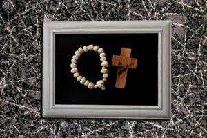 Beads with a white skull and a cross made of rough-textured wood on a black background. White frame photo
