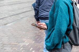 young unrecognizable student girl in blue sweater using smartphone while waiting for bus at bus stop in city, unlimited internet access, photo