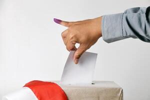 The hand inserts the voting paper into the ballot box with fingers having ink photo