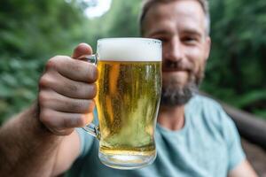 Man holding a mug of beer in the forest. Close-up. photo