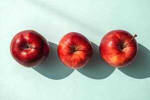 Fresh red apples arranged in a row on a light blue background casting soft shadows in bright sunlight photo