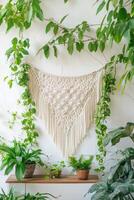 vertical image hand made macrame hanging with intricate pattern with green home plants on shelf and a white textured wall photo