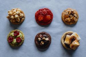 Collection of homemade round cookies with different toppings - raspberry, strawberry, pistachio, caramel, chocolate, peanuts, marshmallow, popcorn. photo