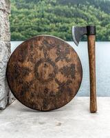 Medieval axe and shield on stone surface near lake photo