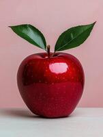Single red apple with green leaves on pink background photo
