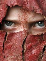 Close up of a face peering through a cracked red surface photo