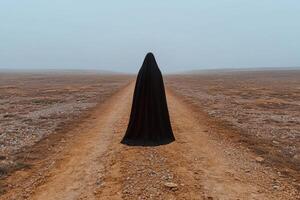 Mysterious figure in black robe standing on a desolate road photo
