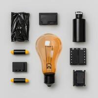 Overhead flatlay of various black tech gadgets and components arranged around a glowing lightbulb on a white background photo