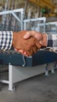 Handshake two diverse engineers on the background of a windows factory video