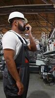 Industrial worker programmer sets up production line conveyor and gives commands via radio walkie talkie video