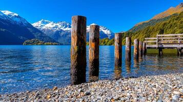 Scenic lake view with wooden posts and snow-capped mountains in the background. photo