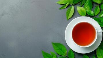 A cup of tea surrounded by fresh green leaves on a textured surface. photo