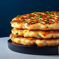 Stacked golden pancakes with green onions on a black plate. photo