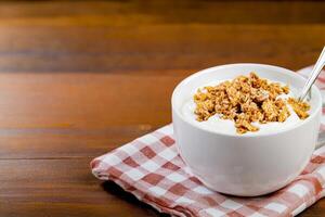 Bowl of yogurt topped with granola on a checkered napkin. photo