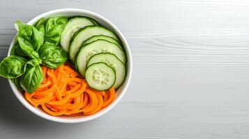 Fresh vegetables in a bowl with spiralized carrots and cucumber slices. photo