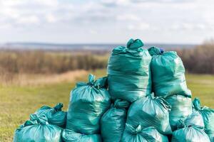 Volunteer for community clean-up concept. Piled green garbage bags in a natural landscape. photo