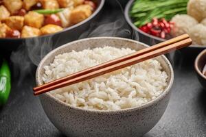 Chinese festive dinner concept. Steaming bowl of rice with chopsticks on a dark surface. photo