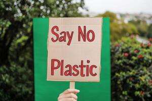 Plastic free campaign. A hand holds a sign that reads Say No Plastic in a green outdoor setting. photo