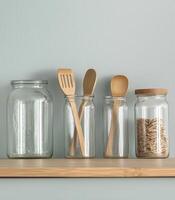 Plastic free campaign. Clear jars and wooden utensils arranged on a wooden shelf against a light wall. photo