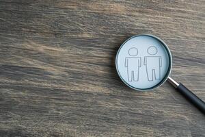 Economic policy reform concept. Magnifying glass focusing on simple human figures on wooden surface. photo