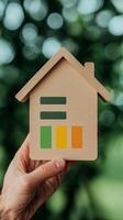 Efficient tech of investment and energy concept. Hand holding a wooden house model with energy efficiency indicators. photo