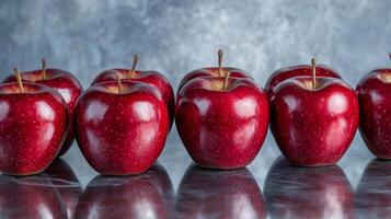 Fresh red apples arranged in a line on a reflective surface. photo