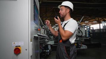 Industrial worker programmer sets up production line conveyor and gives commands via radio walkie talkie video