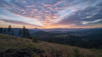 A sunset over a mountain range with a few trees photo
