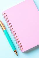 Open notebook with pastel pink pages and mint accents resting on a clean white desk with a teal pen for creative writing and note-taking activities photo