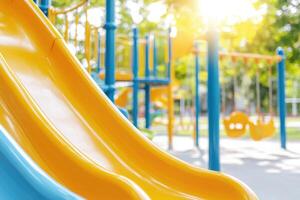 Whimsical playground for children featuring yellow slides and swings surrounded by green trees under bright sunlight photo