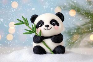 Miniature black-and-white panda holds bamboo on soft felt snow patch with pastel lighting in cozy winter setup photo